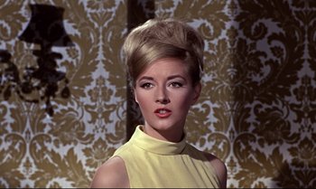 Movie still from “From Russia with Love” (1963), directed by Terence Young – A woman in a yellow dress with a high bun in front of a wall; Close Up shot, Low angle