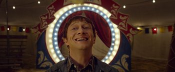 Movie still from “The Walk” (2015), directed by Robert Zemeckis – A man smiling at the camera in front of lights; Close Up shot, Low angle