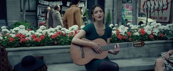 Movie still from “The Walk” (2015), directed by Robert Zemeckis – A woman sitting on the ground holding a guitar; Medium shot, Over the shoulder angle