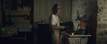 Movie still from “The Walk” (2015), directed by Robert Zemeckis – A man standing in a kitchen preparing food on a stove; Medium shot, Low angle