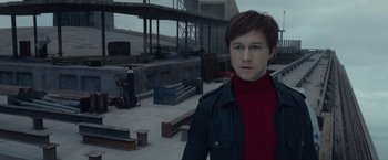 Movie still from “The Walk” (2015), directed by Robert Zemeckis – A man in a red shirt is standing in a parking lot; Medium shot, High angle
