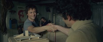 Movie still from “The Walk” (2015), directed by Robert Zemeckis – Two men shaking hands in front of a mirror; Medium shot, Over the shoulder angle