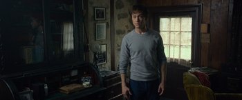 Movie still from “The Walk” (2015), directed by Robert Zemeckis – A man standing in a living room with his hands in his pockets; Medium shot, Over the shoulder angle