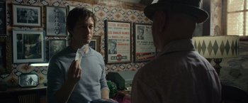 Movie still from “The Walk” (2015), directed by Robert Zemeckis – Two men are sitting in front of a wall of posters; Medium shot, Over the shoulder angle