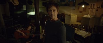 Movie still from “The Walk” (2015), directed by Robert Zemeckis – A young man standing in a room with a guitar; Medium shot, Over the shoulder angle