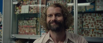 Movie still from “The Walk” (2015), directed by Robert Zemeckis – A man with long hair and a goatee is smiling for the camera; Close Up shot, Low angle