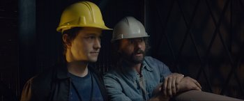 Movie still from “The Walk” (2015), directed by Robert Zemeckis – Two men wearing hard hats are sitting next to each other; Medium shot, Low angle