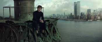 Movie still from “The Walk” (2015), directed by Robert Zemeckis – A man sitting on top of a building next to a body of water; Wide shot, Low angle