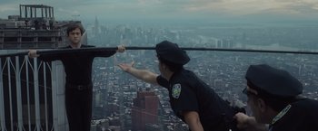 Movie still from “The Walk” (2015), directed by Robert Zemeckis – A man in a police uniform reaching out to grab something from a window; Wide shot, High angle