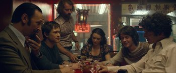 Movie still from “The Walk” (2015), directed by Robert Zemeckis – A group of people sitting around a table; Medium shot, Over the shoulder angle