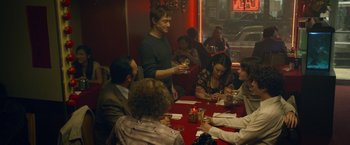 Movie still from “The Walk” (2015), directed by Robert Zemeckis – A group of people sitting at a table with wine glasses; Medium shot, Over the shoulder angle