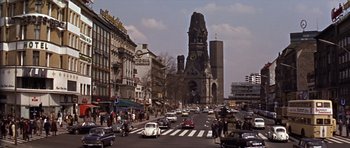 Movie still from “Funeral in Berlin” (1966), directed by Guy Hamilton – A busy city street with cars driving on it; Extreme Wide shot, High angle