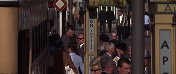 Movie still from “Funeral in Berlin” (1966), directed by Guy Hamilton – A crowd of people walking down a street; Wide shot, High angle