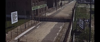 Movie still from “Funeral in Berlin” (1966), directed by Guy Hamilton – An empty street with a sign on the side of the road; Extreme Wide shot, High angle