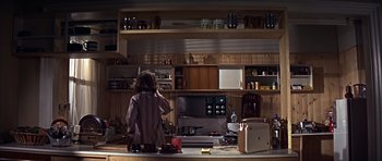 Movie still from “Funeral in Berlin” (1966), directed by Guy Hamilton – A woman standing in a kitchen next to an oven; Wide shot, High angle