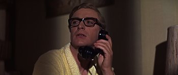 Movie still from “Funeral in Berlin” (1966), directed by Guy Hamilton – A man with glasses talking on a phone; Close Up shot, Low angle