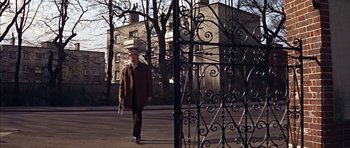 Movie still from “Funeral in Berlin” (1966), directed by Guy Hamilton – A man walking down the street in front of an iron gate; Wide shot, Low angle