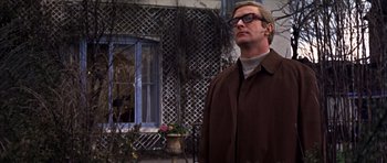 Movie still from “Funeral in Berlin” (1966), directed by Guy Hamilton – A man standing in front of a building with trees; Medium shot, Low angle