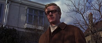 Movie still from “Funeral in Berlin” (1966), directed by Guy Hamilton – A person wearing glasses and a jacket; Close Up shot, Low angle