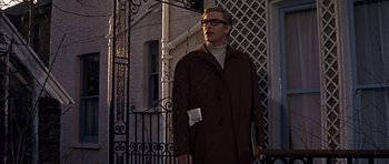 Movie still from “Funeral in Berlin” (1966), directed by Guy Hamilton – A man standing outside of a building holding a cell phone; Medium shot, Low angle