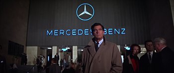 Movie still from “Funeral in Berlin” (1966), directed by Guy Hamilton – A man standing in front of a mercedes - benz sign; Medium shot, Low angle