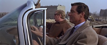 Movie still from “Funeral in Berlin” (1966), directed by Guy Hamilton – Two men are sitting in the back seat of a car; Medium shot, Over the shoulder angle