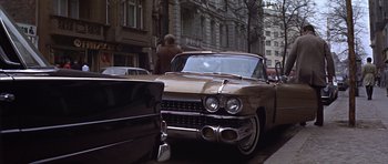 Movie still from “Funeral in Berlin” (1966), directed by Guy Hamilton – An old car parked on the side of the street; Wide shot, Low angle