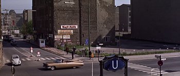 Movie still from “Funeral in Berlin” (1966), directed by Guy Hamilton – A man standing on the side of a road next to a car; Extreme Wide shot, High angle