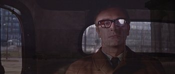 Movie still from “Funeral in Berlin” (1966), directed by Guy Hamilton – A man wearing glasses sitting in the back seat of a car; Close Up shot, Low angle