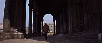 Movie still from “Funeral in Berlin” (1966), directed by Guy Hamilton – A person walking through an archway in an old building; Wide shot, Low angle