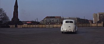 Movie still from “Funeral in Berlin” (1966), directed by Guy Hamilton – An old white truck parked in a parking lot; Wide shot, High angle