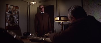 Movie still from “Funeral in Berlin” (1966), directed by Guy Hamilton – A man standing in front of a mirror in front of a lamp; Medium shot, Low angle