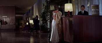 Movie still from “Funeral in Berlin” (1966), directed by Guy Hamilton – A woman in a long white dress standing next to a lamp; Wide shot, Low angle