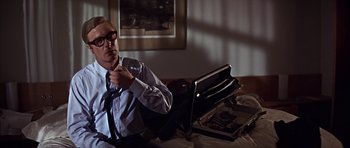 Movie still from “Funeral in Berlin” (1966), directed by Guy Hamilton – A man sitting on a bed tying a tie; Medium shot, High angle