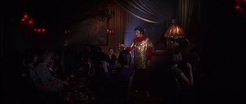 Movie still from “Funeral in Berlin” (1966), directed by Guy Hamilton – A man dressed in a gold and red costume holding a candle in front of a crowd of onlookers; Wide shot, Low angle
