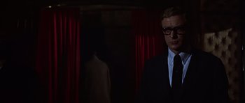 Movie still from “Funeral in Berlin” (1966), directed by Guy Hamilton – A man in a suit and tie standing in front of a red curtain; Close Up shot, Low angle