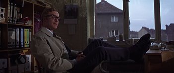 Movie still from “Funeral in Berlin” (1966), directed by Guy Hamilton – A man sitting in a chair in front of a window; Medium shot, Low angle