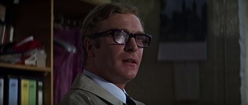 Movie still from “Funeral in Berlin” (1966), directed by Guy Hamilton – A person wearing a suit and glasses; Close Up shot, Low angle