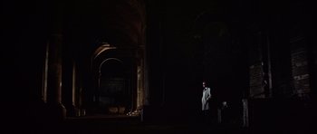 Movie still from “Funeral in Berlin” (1966), directed by Guy Hamilton – A man standing in the dark in front of an archway; Extreme Wide shot, Low angle