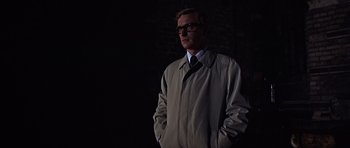 Movie still from “Funeral in Berlin” (1966), directed by Guy Hamilton – A man in a trench coat and tie standing next to a brick wall; Close Up shot, Low angle