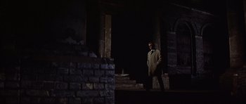 Movie still from “Funeral in Berlin” (1966), directed by Guy Hamilton – A man standing in the dark in front of a brick wall; Wide shot, Low angle