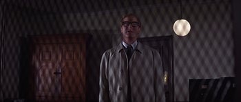 Movie still from “Funeral in Berlin” (1966), directed by Guy Hamilton – A man in a suit and tie standing in front of a fence; Medium shot, Low angle