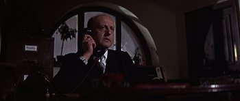 Movie still from “Funeral in Berlin” (1966), directed by Guy Hamilton – An older man talking on a phone in a dark room; Close Up shot, Low angle