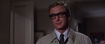 Movie still from “Funeral in Berlin” (1966), directed by Guy Hamilton – A person wearing glasses and a tie; Close Up shot, Low angle