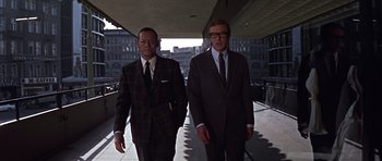 Movie still from “Funeral in Berlin” (1966), directed by Guy Hamilton – A couple of men in suits walking down a sidewalk; Medium shot, Low angle