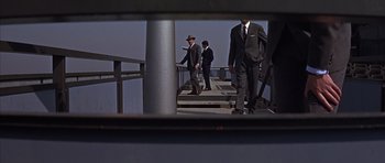 Movie still from “Funeral in Berlin” (1966), directed by Guy Hamilton – A group of men in suits and hats walking down a bridge; Wide shot, Low angle