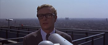 Movie still from “Funeral in Berlin” (1966), directed by Guy Hamilton – A man in a suit and glasses looking through a telescope; Close Up shot, Low angle