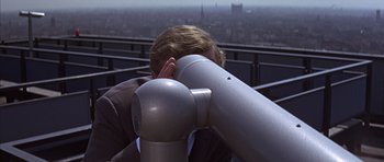 Movie still from “Funeral in Berlin” (1966), directed by Guy Hamilton – A man looking through a telescope; Close Up shot, High angle