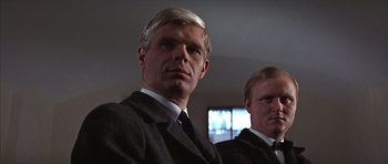 Movie still from “Funeral in Berlin” (1966), directed by Guy Hamilton – A man in a suit and tie standing next to another man in a suit and tie; Close Up shot, Low angle