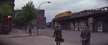 Movie still from “Funeral in Berlin” (1966), directed by Guy Hamilton – A man walking down the street with a suitcase; Wide shot, Low angle